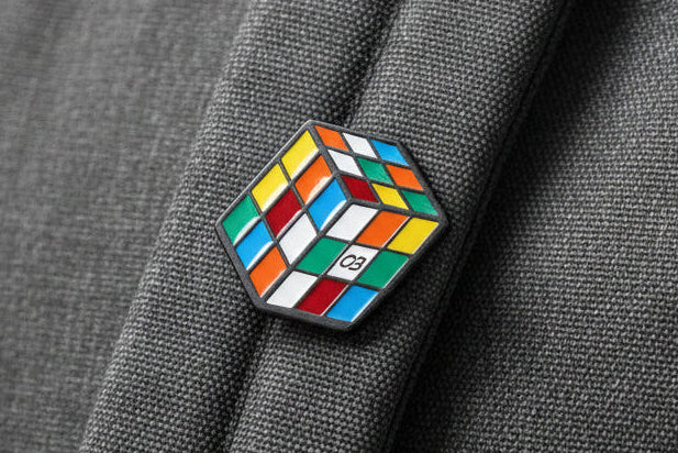 Detalhe do pin de Cubo Mágico metálico com relevo tridimensional do cubo